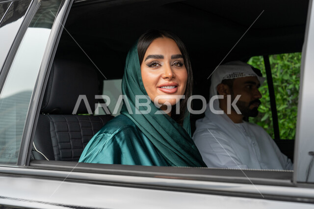 خدمات النقل الآمنة في الإمارات العربية المتحدة, خدمة توصيل الركاب، استخدام التاكسي للوصول إلى الوجهة المطلوبة، صورة مقربة لامرأة عربية خليجية إماراتية ترتدي العباءة الملونة تجلس داخل السيارة مع زوجها وتنظر بإيماءات السعادة والسرور
