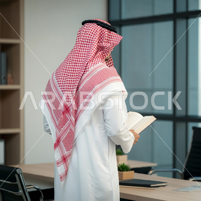الاستمتاع بقراءة الكتب، مهن ووظائف ادارية مكتبية، إدارة شؤون الأعمال وتنظيمها، صورة من الخلف لرجل اعمال عربي خليجي سعودي يرتدي الزي التقليدي والشماغ يقف ويحمل بيده كتاب, ممارسة هواية المطالعة