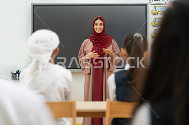 Education objectives in the curricula prescribed for male and female students in the United Arab Emirates, an Arab Gulf Emirati teacher wearing a hijab and abaya explaining lessons to students, a smart school board, participation and interaction in the classroom