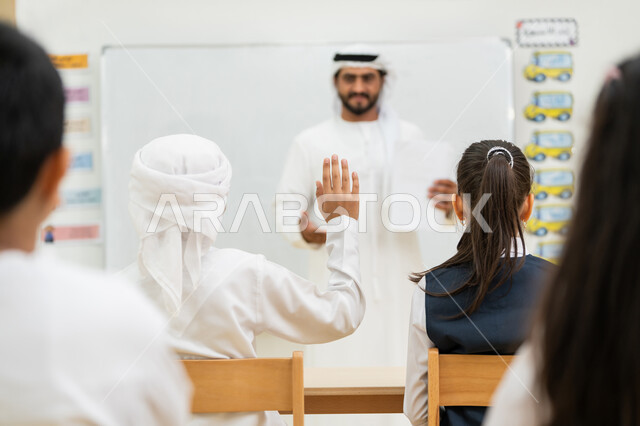 Interaction and activity in the classroom, active participation of students, an Arab Gulf Emirati teacher wearing a kandura and a ghutra explaining the lesson, a white school board, educational objectives in the curricula prescribed for male and female students in the United Arab Emirates