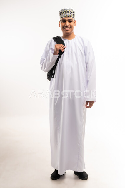 الاستعداد للعام الجامعي الجديد, التعليم العالي في الجامعات والكليات الأكاديمية في سلطنة عمان,    النظر بإيماءات السعادة والسرور, بورتريه لطالب عربي خليجي عماني يرتدي الدشداشة والكمة يحمل حقيبة على ظهره, الجسم بالطول الكامل، خلفية بيضاء