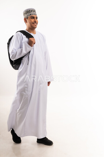 الاستعداد للعام الجامعي الجديد, التعليم العالي في الجامعات والكليات الأكاديمية في سلطنة عمان,    النظر بإيماءات السعادة والسرور, بورتريه لطالب عربي خليجي عماني يرتدي الدشداشة والكمة يحمل حقيبة على ظهره, الجسم بالطول الكامل، خلفية بيضاء