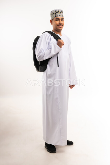 الاستعداد للعام الجامعي الجديد, التعليم العالي في الجامعات والكليات الأكاديمية في سلطنة عمان,    النظر بإيماءات السعادة والسرور, بورتريه لطالب عربي خليجي عماني يرتدي الدشداشة والكمة يحمل حقيبة على ظهره, الجسم بالطول الكامل، خلفية بيضاء