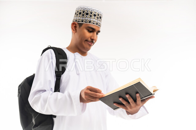 الاهتمام بتصفح الكتب المفيدة، حب المطالعة والقراءة، التعليم الجامعي في سلطنة عمان, مراجعة الدروس اليومية, مفهوم الاجتهاد والتفوق, بورتريه لطالب جامعي عربي خليجي عماني يرتدي الدشداشة والكمة يحمل حقيبة على ظهره وبيده كتاب ويقوم بدراسة المحاضرات, خلفية بيضاء