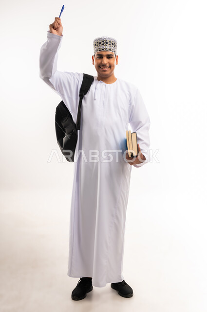 الإستعداد للكتابة وتحديد شيء ما, تدوين وتسجيل الملاحظات، بورتريه مقرب لشاب عربي خليجي عماني يرتدي الدشداشة والكمه يمسك بيده قلم يكتب شيء ما, مفهوم التعليم بالمناهج المقررة، خلفية بيضاء