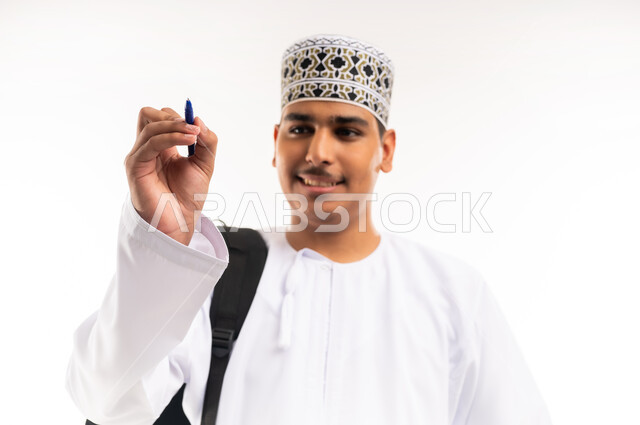 الإستعداد للكتابة وتحديد شيء ما, تدوين وتسجيل الملاحظات، بورتريه مقرب لشاب عربي خليجي عماني يرتدي الدشداشة والكمه يمسك بيده قلم يكتب شيء ما, مفهوم التعليم بالمناهج المقررة، خلفية بيضاء