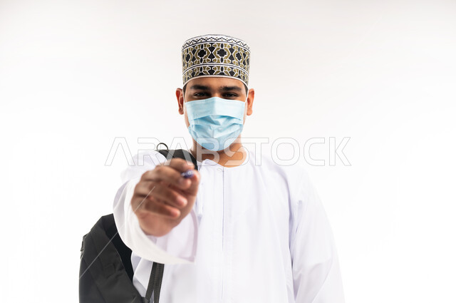 Preparing to write and outline something, taking notes, close-up portrait of a young Omani Gulf Arab man wearing a dishdasha and a sleeve holding a pen in his hand writing something, concept of education with prescribed curricula, white background