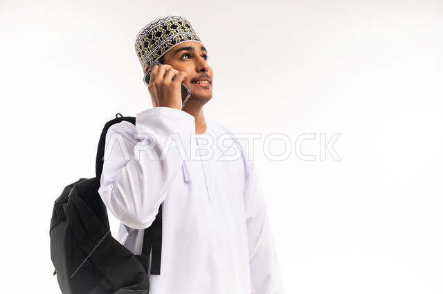 الدردشة مع الأهل والأصدقاء، تسهيل التواصل مع الآخرين باستخدام الهاتف المحمول، تطورات تقنية وتكنولوجية، بورتريه لرجل عماني شايب يرتدي الدشداشة والكمه يقوم بالمحادثة مع الأقارب عبر الموبايل، خلفية بيضاء