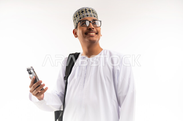 الاستفادة من الأجهزة والتكنولوجيا الحديثة في الاطمئنان على الأقارب، التواصل مع الأهل والأصدقاء وسماع أخبارهم،  بورتريه  مقرب لرجل عربي خليجي عماني يرتدي الدشداشة والكمه ويمسك الهاتف المحمول ينظر الى الاعلى بإيماءات السعادة،  خلفية بيضاء