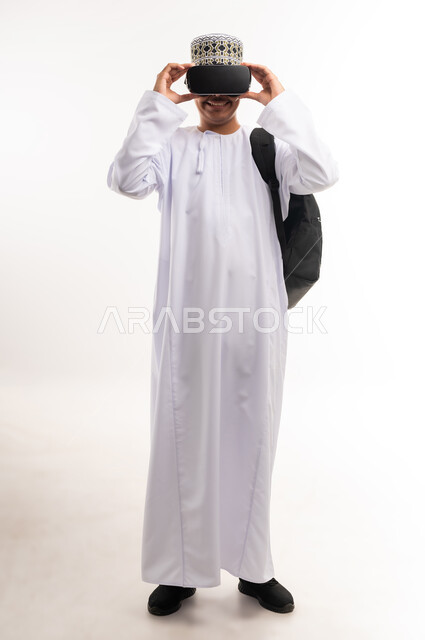 الاندماج والتفاعل مع العالم الخيالي، استخدام التقنيات والتكنولوجيا المتطورة، بورتريه لشاب عربي خليجي عماني يرتدي الدشداشة والكمه العمانية يضع نظارة في آر على عينيه، مشاهدة أفلام الواقع الافتراضي، قضاء أوقات الفراغ بشكل ممتع، خلفية بيضاء