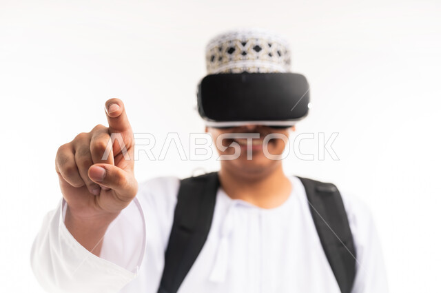 النقر على الشاشة ومحاولة لمس عنصر ما, التفاعل ومحاكاة العالم الخيالي, بورتريه مقرب لشاب عربي خليجي عماني يرتدي الدشداشه والكمه يضع نظارة الواقع الافتراضي, الاستمتاع بمشاهدة الافلام ثلاثية الابعاد, قضاء أوقات الفراغ بالأنشطة الالكترونية المسلية, خلفية بيضاء