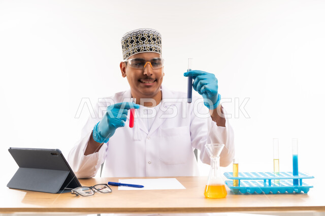 التفاعلات الكيميائية داخل المختبر, اجراء التجارب العلمية, اسخدام انابيب الاختبار الزجاجية, دمج التعليم مع التقنية والتكنولوجيا, بورتريه مقرب لطالب جامعي عربي خليجي عماني يرتدي الكمه والدشداشه يجلس في معمل الكيمياء, التعليم الاكاديمي في سلطنة عمان, خلفية بيضاء