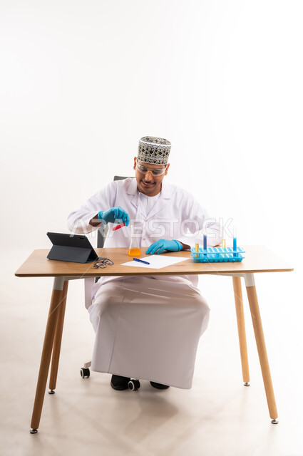 Integrating education with technology, using test tubes to conduct experiments in the laboratory, searching for the results of chemical reactions, the concept of biochemistry, portrait of an Arab Gulf Omani university student wearing a dishdasha and a kimono sitting in a chemistry lab, white background