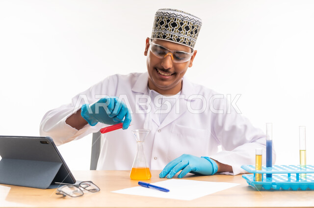 استخدام أنابيب الاختبار لإجراء التجارب في المختبر, البحث عن نتائج التفاعلات الكيميائية, مفهوم الكيمياء الحيوية, بورتريه مقرب لطالب جامعي عربي خليجي عماني يرتدي الدشداشه والكمه يجلس في معمل الكيمياء, دمج التعليم مع التقنية والتكنوجيا, خلفية بيضاء