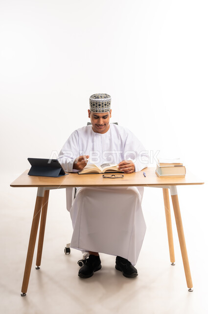 دمج التعلم مع التقنية والتكنولوجيا, قراءة ومتابعة الدروس اليومية, بورتريه لطالب جامعي عربي خليجي عماني يرتدي الكمه والدشداشه يقوم بقراءة الكتاب, المناهج والمواد التعليمية, مفهوم التعليم الالكتروني في الجامعات الاكاديمية في سلطنة عمان, خلفية بيضاء