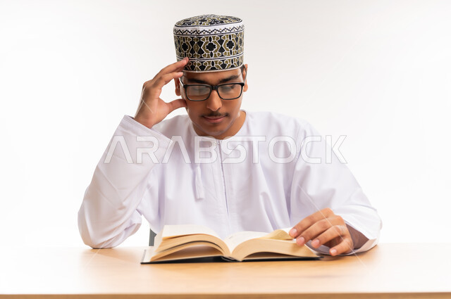 الاستمتاع بممارسة هواية المطالعة, بورتريه مقرب لطالب جامعي عربي خليجي عماني يرتدي الدشداشه والكمه والنظارة الطبية يقوم بقراءة الكتاب, قضاء أوقات الفراغ بالأنشطة المفيدة, مفهوم التعلم والتفوق والاجتهاد, المناهج والمواد التعليمية في سلطنة عمان, خلفية بيضاء