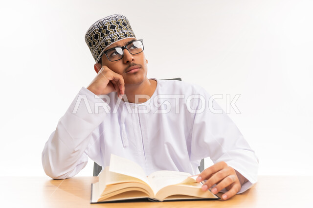 قضاء أوقات الفراغ بالأنشطة المفيدة, المناهج والمواد التعليمية في سلطنة عمان, محاولة تذكر شيء ما, الاستمتاع بممارسة هواية المطالعة, بورتريه مقرب لطالب جامعي عربي خليجي عماني يرتدي الدشداشه والكمه والنظارة الطبية ينظر إلى شيء معين, خلفية بيضاء