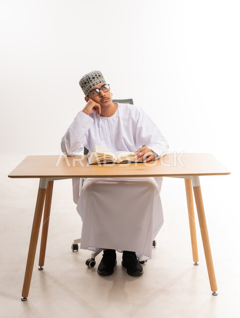 محاولة تذكر شيء ما, الاستمتاع بممارسة هواية المطالعة, بورتريه لطالب جامعي عربي خليجي عماني يرتدي الدشداشه والكمه والنظارة الطبية ينظر إلى شيء معين, قضاء أوقات الفراغ بالأنشطة المفيدة, المناهج والمواد التعليمية في سلطنة عمان, خلفية بيضاء