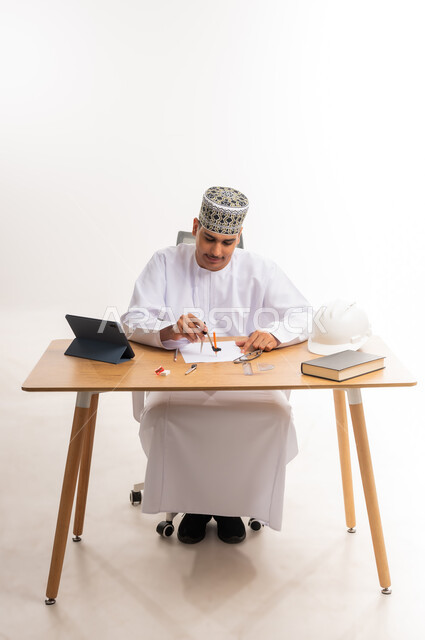 دمج التقنيات الحديثة والتكنولوجيا بالتعليم الأكاديمي, مفهوم الاجتهاد والتفوق, المناهج والمواد التعليمية, بورتريه لطالب جامعي عربي خليجي يرتدي الدشداشه والكمه يجلس على الطاولة في مكتبة الجامعة ويقوم بالرسم الهندسي باستخدام الفرجار, خلفية بيضاء