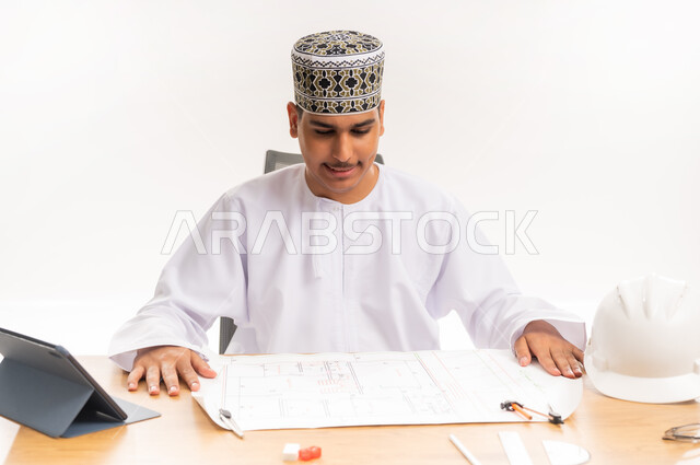 الدراسة و الاجتهاد والتفوق, المناهج والمواد التعليمية، التعليم الجامعي في سلطنة عمان, بورتريه مقرب لطالب جامعي عربي خليجي عماني يرتدي الكمه والدشداشه يقوم بدراسة وتصميم المشروع الهندسي, مفهوم الهندسة والانشاء, دمج التكنولوجيا في المجال التعليمي، خلفية بيضاء