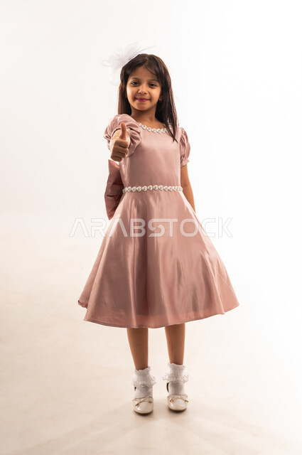 علامة الجودة والامتياز، المناسبات والأعياد الدينية، فتاة عربية خليجية عمانية مبتسمة ترتدي لباس العيد الأنيق ترفع إبهامها للأعلى بإيماءات الإعجاب والموافقة، الاحتفال بعيد الفطر السعيد، الاهتمام بالجمال والمظهر الخارجي، الجسم بالطول الكامل، خلفية بيضاء