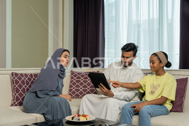 A smiling and happy Emirati Gulf Arab family, using modern advanced devices and technologies, watching movies and electronic stories via a tablet, familiarity, harmony and affection between family members, spending a fun time with the children