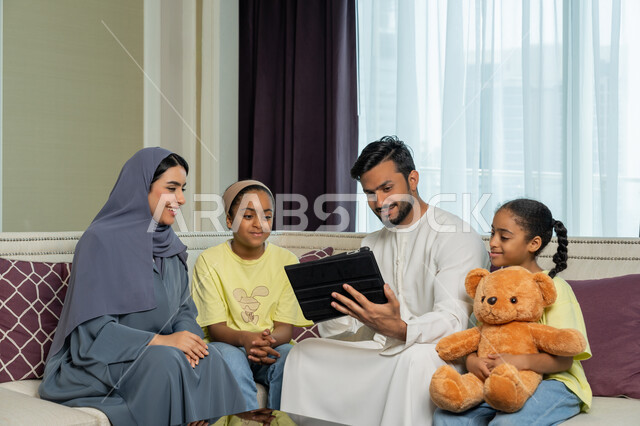 استخدام الاجهزة والتقنيات الحديثة المتطورة, مشاهدة الافلام والقصص الالكترونية عبر جهاز التابليت اللوحي، الالفة والانسجام والمودة بين افراد الاسرة، عائلة عربية خليجية اماراتية مبتسمة وسعيدة، قضاء وقت ممتع مع الاولاد