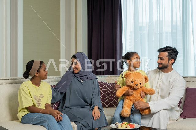مفهوم الأمان والإستقرار العائلي، أجواء عائليه سعيده مليئه بالحب والحنان، أسره عربيه خليجيه اماراتيه تجلس في غرفه المعيشه، ايماءات الفرح والسعاده لقضاء أوقات ممتعه مع الأهل، الألفه والمحبه بين الآباء والابناء