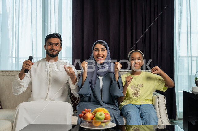 متابعه المنتخب الوطني الاماراتي، رفع قبضة اليد للاعلى بايماءات الحماس والفرحة بالإنتصار، الاستمتاع في قضاء الوقت مع الأهل، عائله عربيه خليجيه اماراتيه تجلس في غرفه المعيشه تقوم بمشاهدة المباراة عبر التلفاز، شغف تشجيع فريق كره القدم المفضل