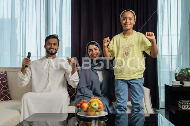 الاستمتاع في قضاء الوقت مع الأهل، رفع قبضة اليد للاعلى بايماءات الحماس والفرحة بالإنتصار، عائله عربيه خليجيه اماراتيه تجلس في غرفه المعيشه تقوم بمشاهدة المباراة عبر التلفاز، شغف تشجيع فريق كره القدم المفضل، متابعه المنتخب الوطني الاماراتي