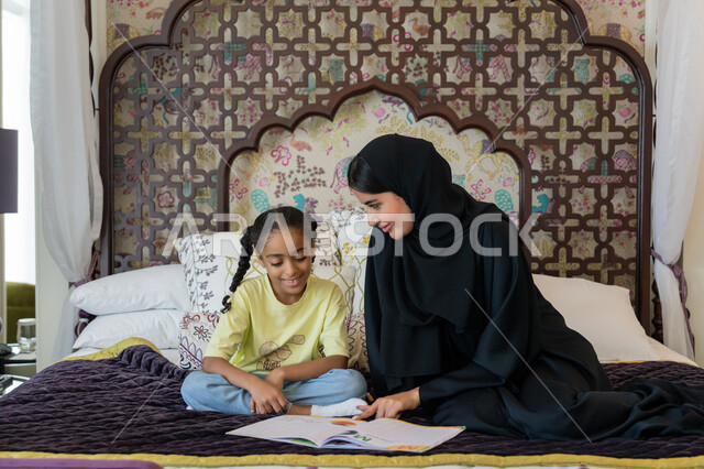 الديكورات والتصاميم الداخلية لغرف النوم في الامارات العربية المتحدة, تنمية قدرات و مهارات الطفل, فتاة عربية خليجية اماراتية مبتسمة ترتدي الزي الكاجوال تجلس على السرير تقوم بحل واجباتها المنزلية مع والدتها, ايماءات السرور و الفرح
