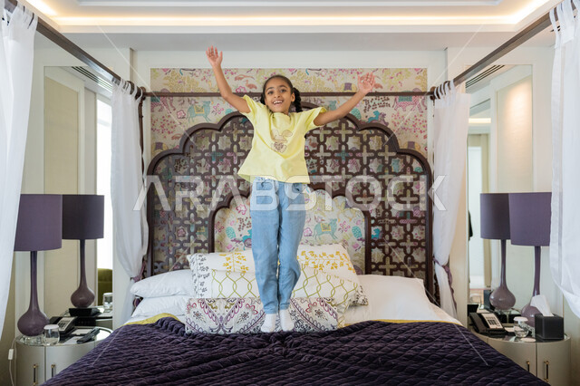 Decorations and interior designs of hotel bedrooms in the United Arab Emirates, having a good time playing and having fun, a Saudi girl practicing recreational activities, an Arab Gulf Emirati girl playing on the bed, gestures of happiness and joy
