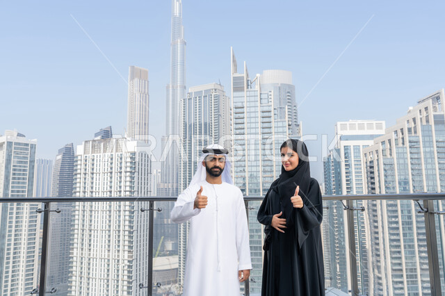 تعابير الجودة والامتياز، موظفين عربيين خليجيان اماراتيين يقفان باستقمامة يرفعان اصبعهما السبابة للاعلى بايماءات القبول والموافقة، بيئة العمل المريحة في شركات الامارات، التفاهم والتعاون بين الزملاء لتحقيق أهداف الشركة، خلفية الأبراج وناطحات السحاب في الامارات العربية المتحدة