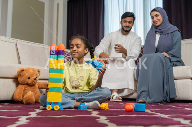 Spending quality time with children, developing the child's abilities and skills, familiarity, harmony and affection between family members, enjoying the summer vacation, an Arab Gulf Emirati couple looking at their children with expressions of love and happiness, fun educational and entertaining games, supporting and encouraging children