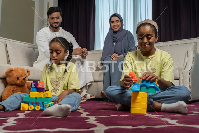 الاستمتاع بالعطلة الصيفية, الالفة والانسجام والمودة بين افراد الاسرة، قضاء وقت ممتع مع الاولاد، تنمية قدرات و مهارات الطفل, زوجان عربيان خليجيان اماراتيان ينظران الى ولديهما بتعابير الحب والسعادة, العاب تعليمية ترفيهية ممتعة,مساندة الأبناء و تشجيعهم