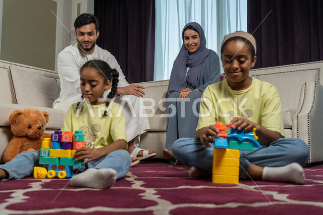 تنمية قدرات و مهارات الطفل, زوجان عربيان خليجيان اماراتيان ينظران الى ولديهما بتعابير الحب والسعادة, العاب تعليمية ترفيهية ممتعة, الاستمتاع بالعطلة الصيفية, الالفة والانسجام والمودة بين افراد الاسرة، قضاء وقت ممتع مع الاولاد، مساندة الأبناء و تشجيعهم