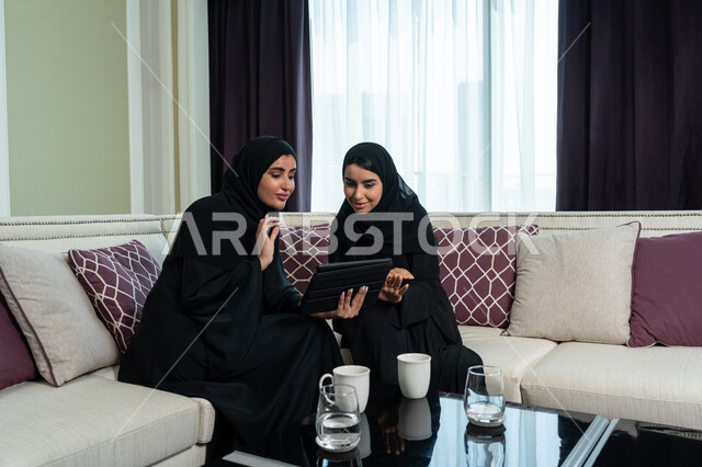 مفهوم إدارة شؤون الأعمال وتنظيمها, استخدام الاجهزة و التقنيات الحديثة المتطورة, الإشراف والتدقيق وتحقيق الاهداف, ايماءات التركيز و الاندماج, سيدة اعمال عربية خليجية اماراتية محجبة ترتدي العباءة السوداء تقوم بتوضيح مهام العمل للموظفة عبر جهاز التابليت اللوحي