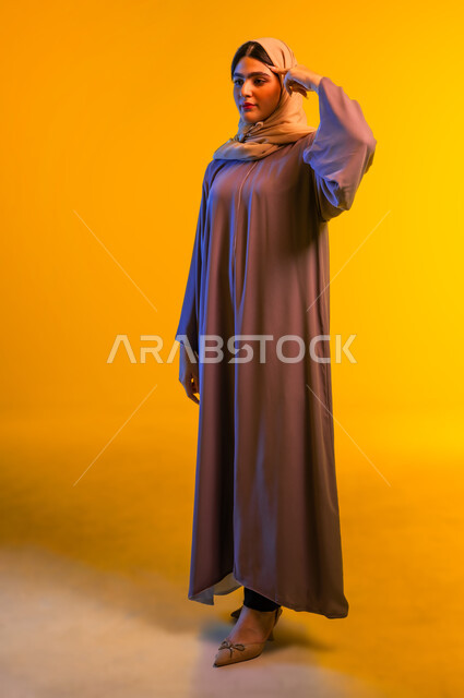 Saudi woman trying to figure something out, thinking and making decisions, portrait of young Arab Gulf Omani woman wearing abaya and hijab putting index finger on her head with gestures of not remembering, full body, yellow background