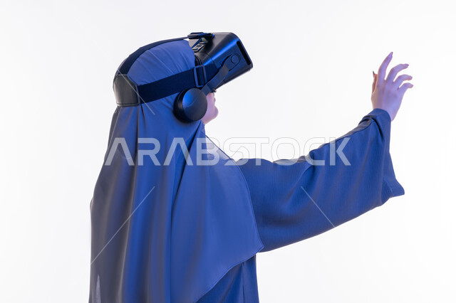 الاندماج ومحاكاة العالم الخيالي، المتعة و التسلية بالمشاهدة عبر نظارة الواقع الافتراضي، بورتريه مقرب من الجانب لإمرأة عربية خليجية إماراتية محجبة ترتدي العباءة وتنظر من خلال نظارات ثلاثية الأبعاد، شابة سعودية ترفع كف يديها للاعلى لمحاولة لمس شيء ما، خلفيه بيضاء