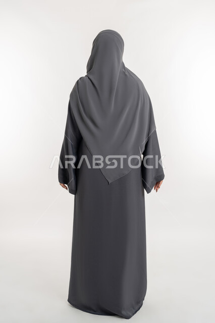 النظرة المستقبلية والتفكير لتحقيق النجاح, التمعن وإيجاد حل لموضوع ما, الاهتمام بالمظهر الخارجي، مفهوم الأناقة والأنوثة، بورتريه من الخلف لإمرأة عربية خليجية إماراتية ترتدي العباءة والحجاب، شابة سعودية تنظر إلى شيء ما, الطول الكامل للجسم, خلفية بيضاء