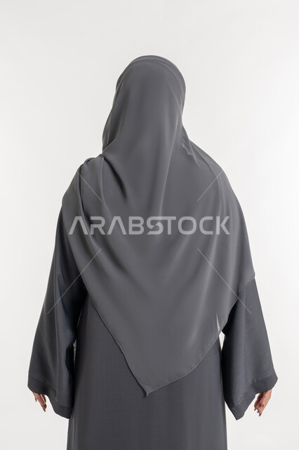 Contemplating and finding a solution to a topic, caring about one's appearance, the concept of elegance and femininity, a portrait from the back of an Arab Gulf Emirati woman wearing an abaya and hijab, a young Saudi woman looking at something, a future outlook and thinking to achieve success, white background