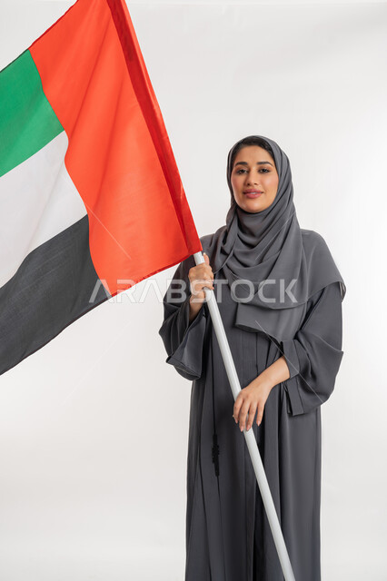 هوية اليوم الوطني الاماراتي 51، احياء ذكرى استقلال الإمارات، بورتريه لامراة عربية خليجية إماراتية ترتدي العباءة تقوم بحمل علم الإمارات، الحب والانتماء للوطن، النظر الى الكاميرا بايماءات الاعتزاز والثقة، خلفية بيضاء