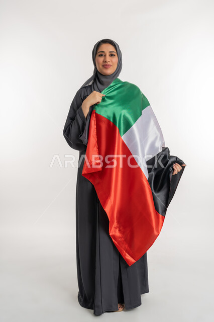Pride and honor of the nation's achievements, celebrating the UAE National Day on December 2, portrait of an Arab Gulf Emirati woman wearing an abaya carrying the UAE flag on her shoulder, celebrating the UAE National Day, national holidays and occasions, full body length, white background