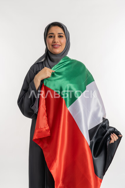 مفهوم الحب والانتماء للبلاد, الاحتفال باليوم الوطني الإماراتي, الأعياد و المناسبات الوطنية, الاعتزاز والفخر بإنجازات الوطن، الاحتفال بالعيد الوطني الإماراتي 2 ديسمبر،  بورتريه لامراة عربية خليجية إماراتية ترتدي العباءة تحمل علم الامارات على كتفها، خلفية بيضاء