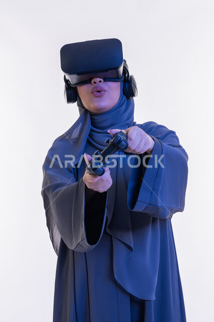 ايماءات الاندماج مع الجيم،  قضاء وقت ممتع بالألعاب الالكترونية الترفيهية، دمج التسلية مع العالم الخيالي، بورتريه لإمرأة عربية خليجية إماراتية محجبة ترتدي العباءة ونظارة الواقع الإفتراضي تمسك عصا التحكم، شابة سعودية تستخدم الأجهزة والتقنيات الحديثة، خلفية بيضاء