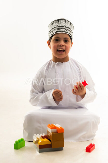 Omani society's interest in people with disabilities, recreational activities for people with special needs, portrait of an Omani Gulf Arab boy with Down syndrome wearing a dishdasha and a kimono assembling cube pieces, developing the mental abilities of the disabled, white background