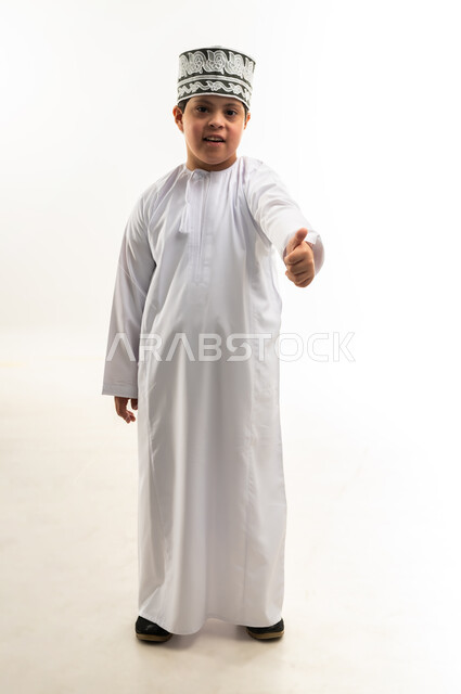 تعابير القبول والموافقة، مفهوم الاناقة والاهتمام بالمظهر الخارجي, بورتريه لولد عربي خليجي عماني يرتدي الدشداشة و الكمه يرفع يده بايماءات الاعجاب والرضى، صورة الجسم بالطول الكامل, خلفية بيضاء