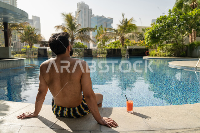 الاستمتاع بالمشروبات البارد المنعشة, ممارسة رياضة السباحة الممتعة, الجلوس والاسترخاء في المسبح, مفهوم الاستجمام والاختلاء, شاب عربي خليجي إماراتي يجلس داخل حوض السباحة في إحدى المنتجعات السياحية بالإمارات, القيام بالأنشطة الترفيهية المسلية