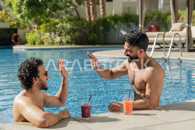 الاستمتاع بالمشروبات الباردة المنعشة, القيام بالأنشطة الترفيهية المسلية, مشاركة الأصدقاء اللحظات الممتعة, قضاء العطلة الصيفية في المنتجعات السياحية, شابان عربيان خليجيان إماراتيان يجلسان داخل حوض السباحة في إحدى الفنادق بالإمارات