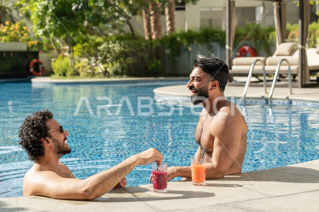 الاستمتاع بالمشروبات الباردة المنعشة, القيام بالأنشطة الترفيهية المسلية, مشاركة الأصدقاء اللحظات الممتعة, قضاء العطلة الصيفية في المنتجعات السياحية, شابان عربيان خليجيان إماراتيان يجلسان داخل حوض السباحة في إحدى الفنادق بالإمارات